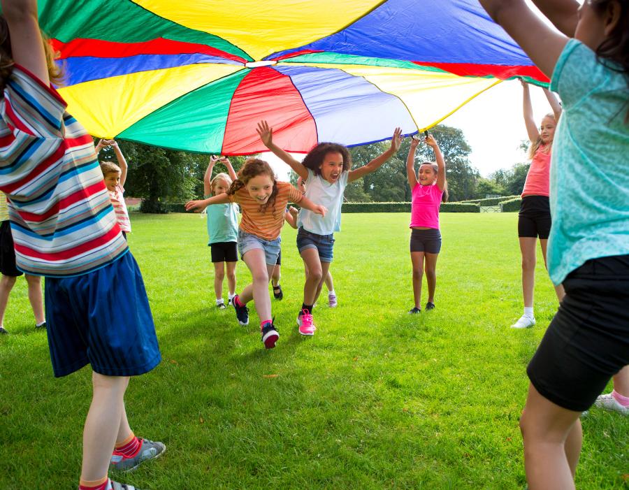 Children in a sunny field playing under a parachute