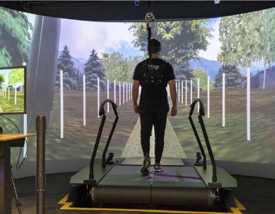 man walks on treadmill in front of large screen with digital environment displayed