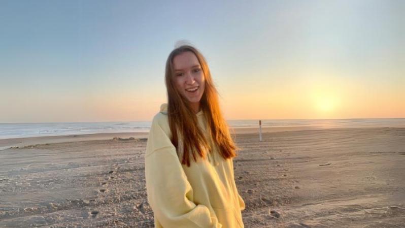 portrait of person with long hair wearing yellow hoodie on the beach