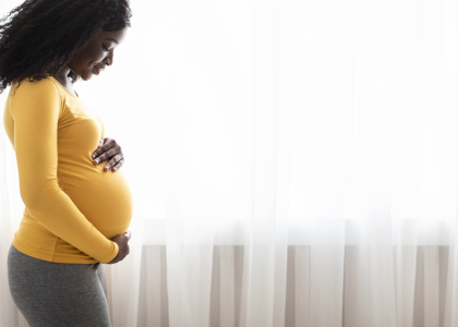 Black pregnant woman standing by window with hands on her belly