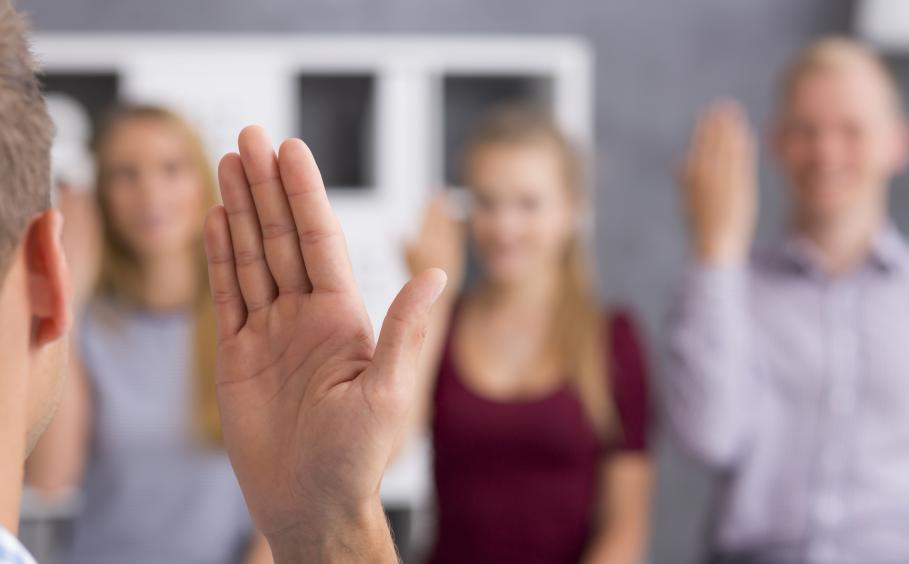 Close up of a hand in a welcome gesture, in the background blurred image of three people