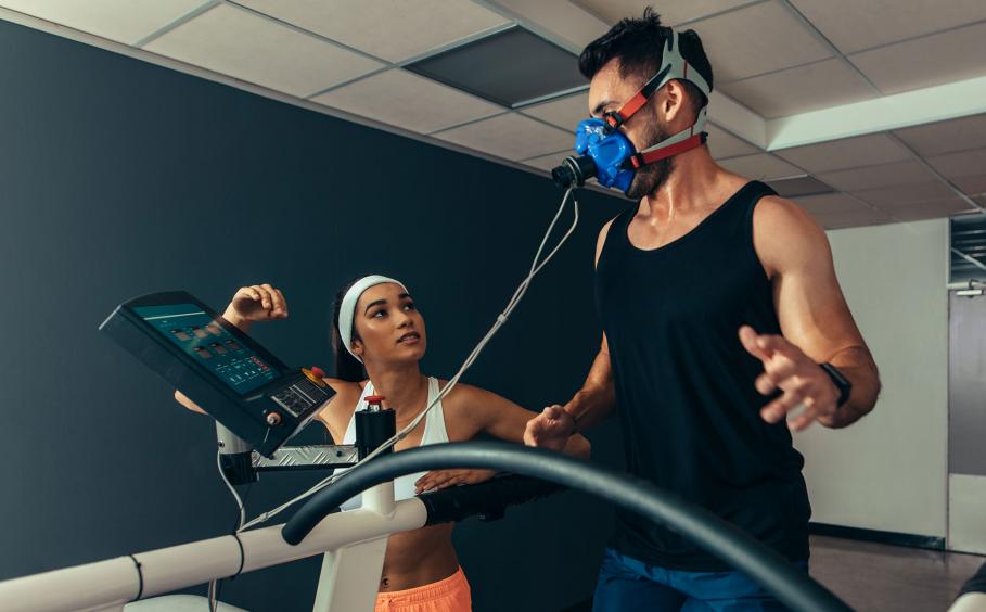 Woman monitoring runner with mask on treadmill in laboratory