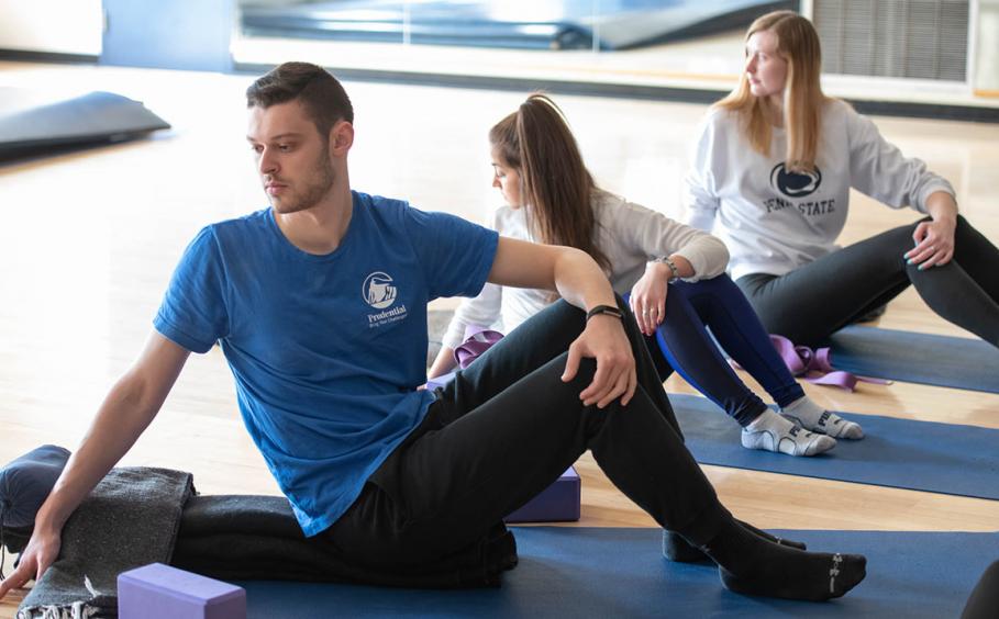 A male student and two female students in a yoga class. 