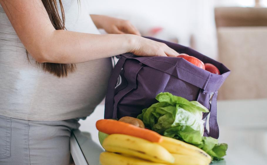 A pregnant woman unpacking fruits and vegetables. 